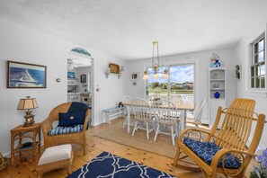 A room with a dining table, chairs, wicker furniture, a rug, and a view of the outdoors. - East Sandwich Beach Escape with Marsh Views (East Sandwich)