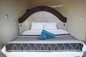 A bed with a headboard, two pillows, a blanket, and a rolled towel.
