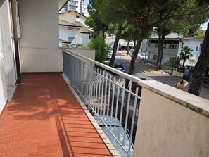 Ein Balkon mit roten Fliesen, einem Metallgeländer und Blick auf eine Straße mit Bäumen und Gebäuden.