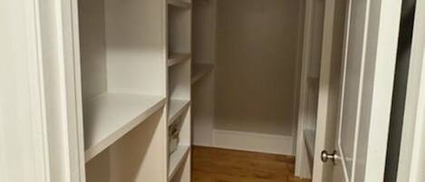 A narrow hallway with white closet doors and shelves, wooden flooring, and a white wall.
