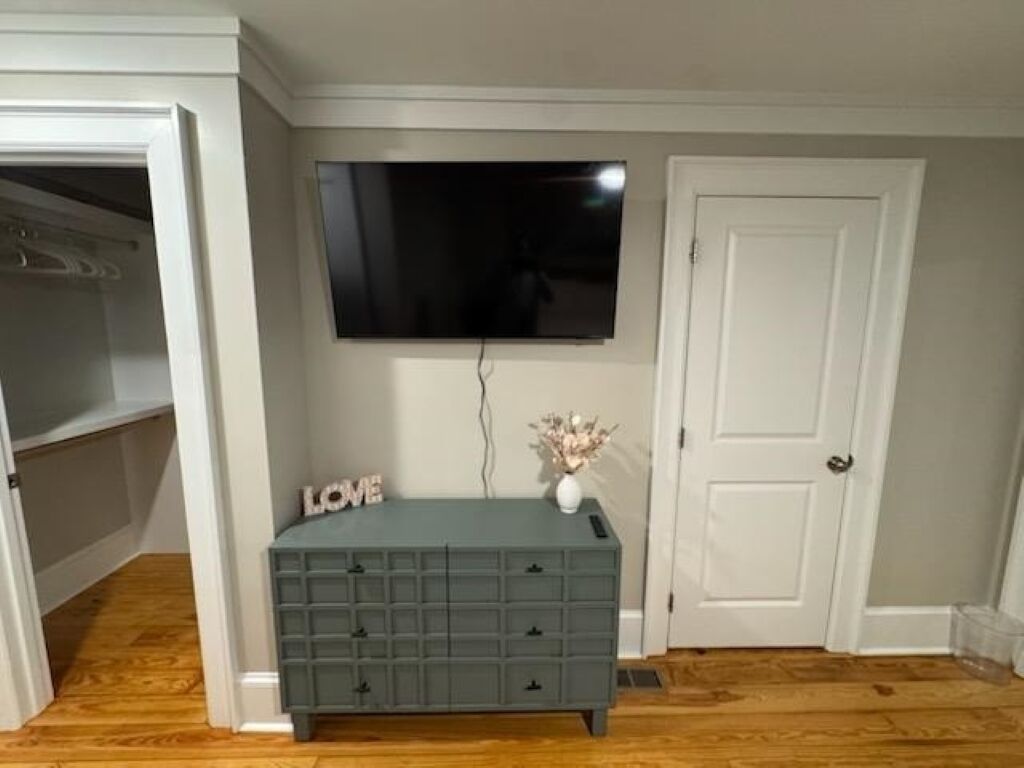 Une pièce avec une commode grise, un téléviseur à écran plat fixé au mur et une porte blanche.