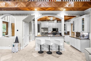 A modern kitchen with white cabinetry, a central island with bar stools, and a herringbone wooden ceiling.