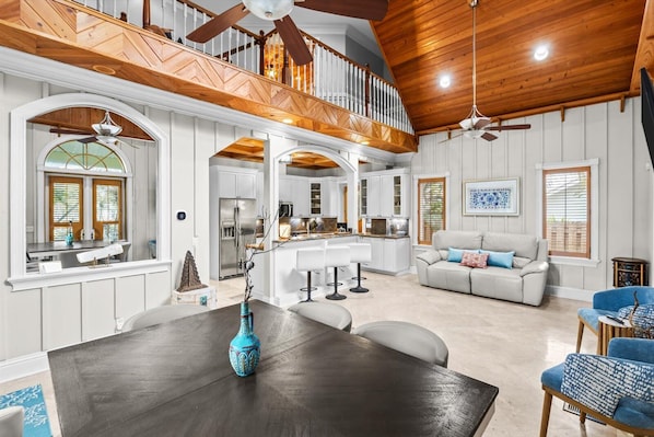 A spacious living area with a high ceiling, wooden beams, a dining table, and a sofa.
