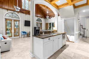 A spacious kitchen with a central island, wooden ceiling beams, and a large window.