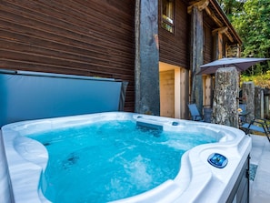 Un jacuzzi con panel de control, zona cubierta y un pilar de piedra.