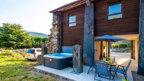 Une maison moderne avec un mur en pierre, un jacuzzi, un espace salon extérieur et une voiture garée à proximité.