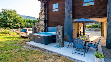 Una casa moderna con un muro de piedra, un jacuzzi, mobiliario exterior y un coche aparcado cerca.