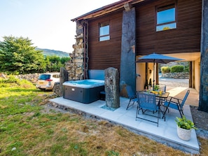 Una casa moderna con un muro de piedra, un jacuzzi, mobiliario exterior y un coche aparcado cerca.