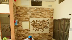 A reception desk with a patterned wall behind it, a potted plant, and a person seated at the desk. - The Grand Ganga Paying Guest (VARANASI)