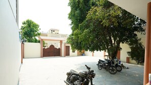 A courtyard with two motorcycles parked, a tree, and a building with a gate in the background. - The Grand Ganga Paying Guest (VARANASI)