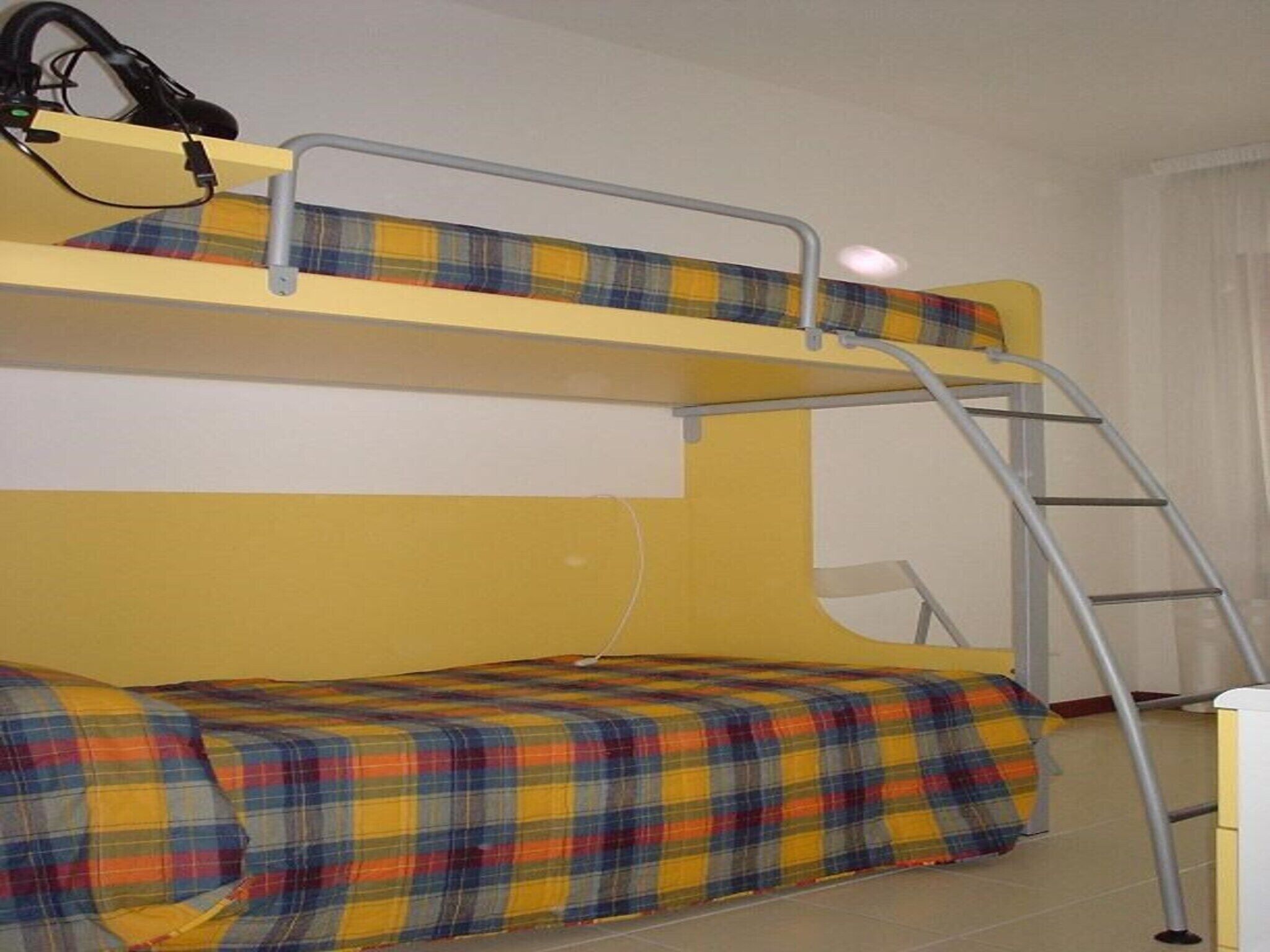 Un lit superposé avec une échelle, une couverture à carreaux et un mur blanc.