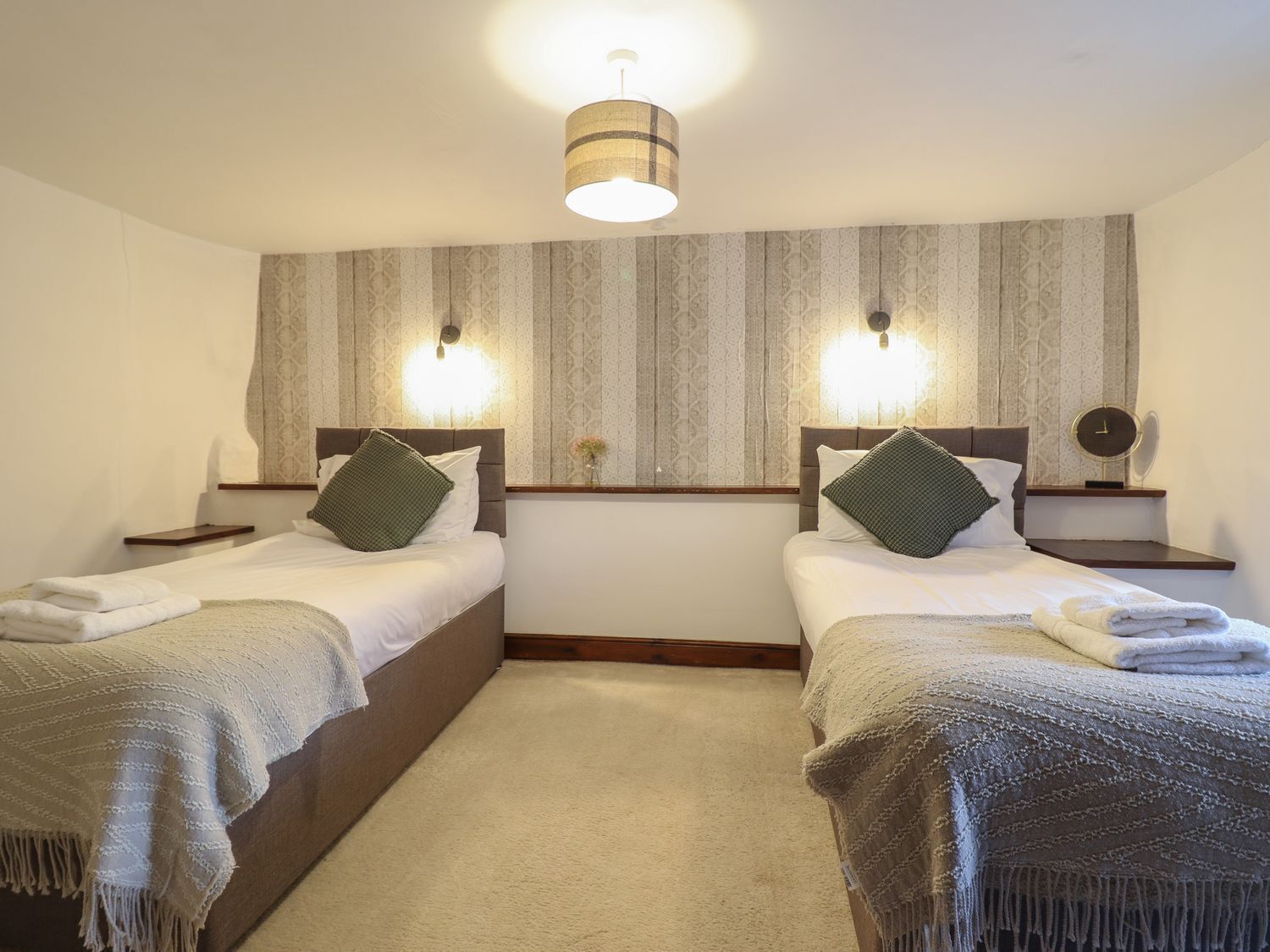 Habitación doble con dos camas, cada una con cabecera, mesitas de noche, lámparas y espejo.