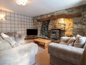 A cozy living room with a stone fireplace, a flat-screen TV, and plaid-patterned furniture. - Cader Cottage (Dolgellau)
