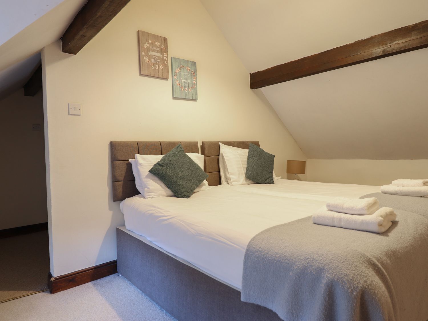 A bedroom with a sloped ceiling, a bed with white linens, two pillows, and a blanket.