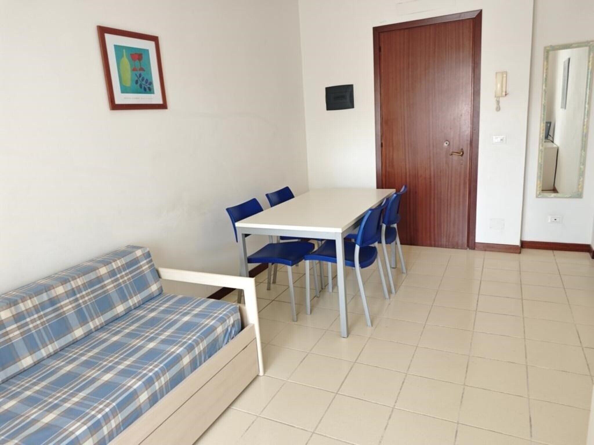 Een kamer met een bank, een tafel met stoelen, een houten deur en een lijst met een afbeelding aan de muur.