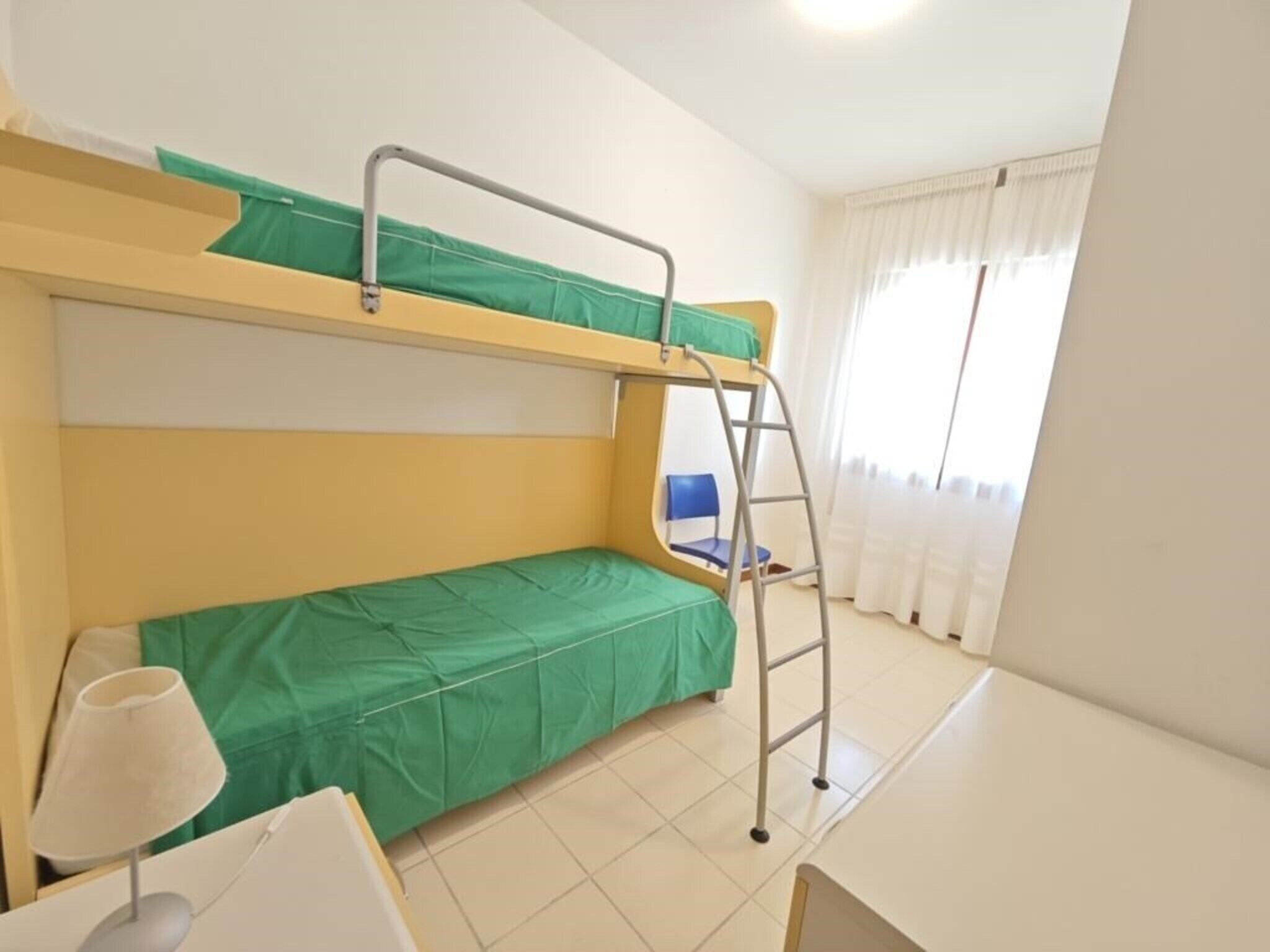 Habitación con literas, escritorio, silla, una escalera y una ventana con cortinas.