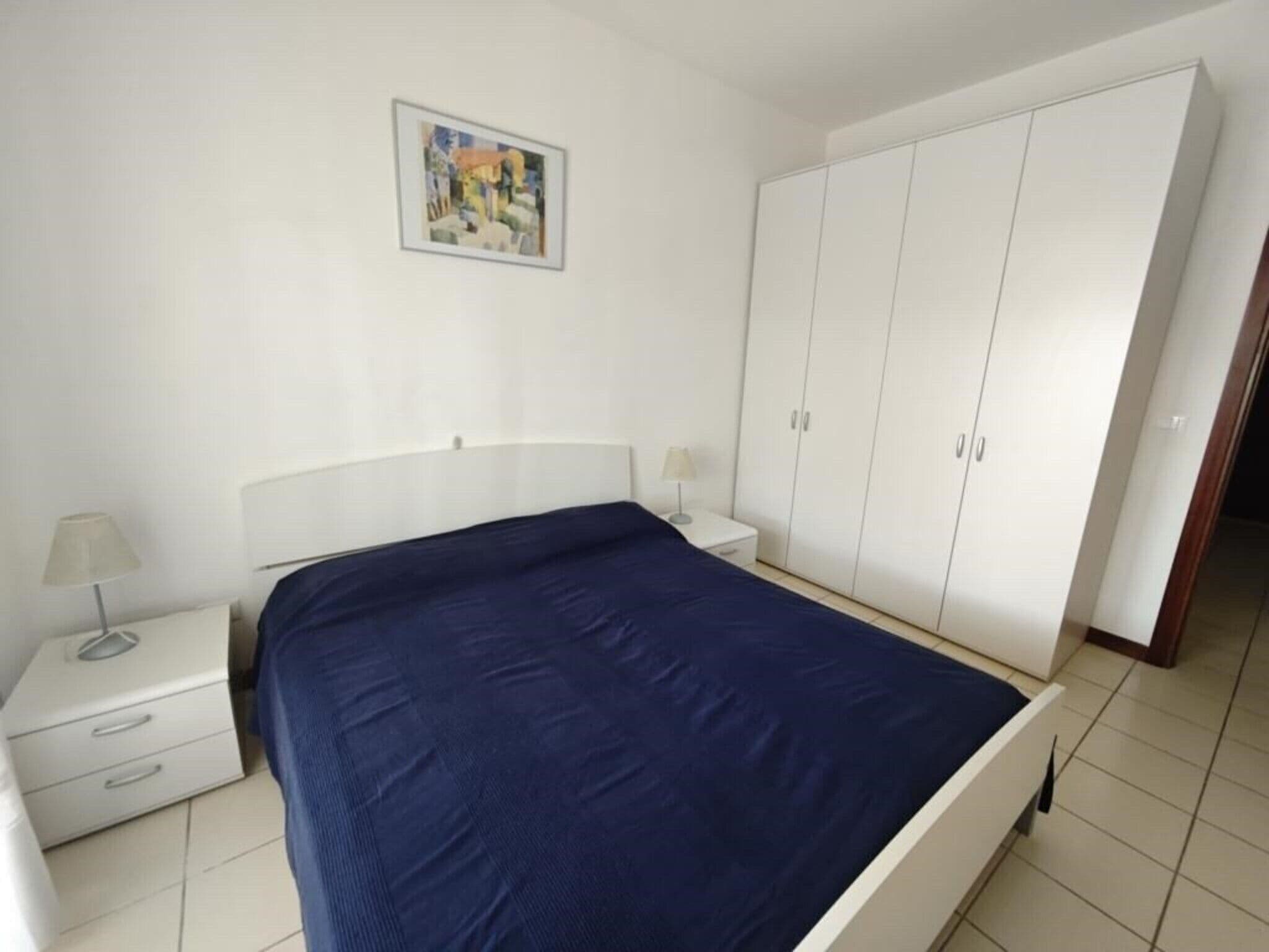 Une chambre à coucher avec un lit, une table de chevet, une lampe, une armoire et un tableau au mur.