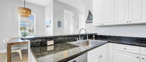 A modern kitchen with white cabinets, granite countertops, a dishwasher, and a dining area with a table and chairs.