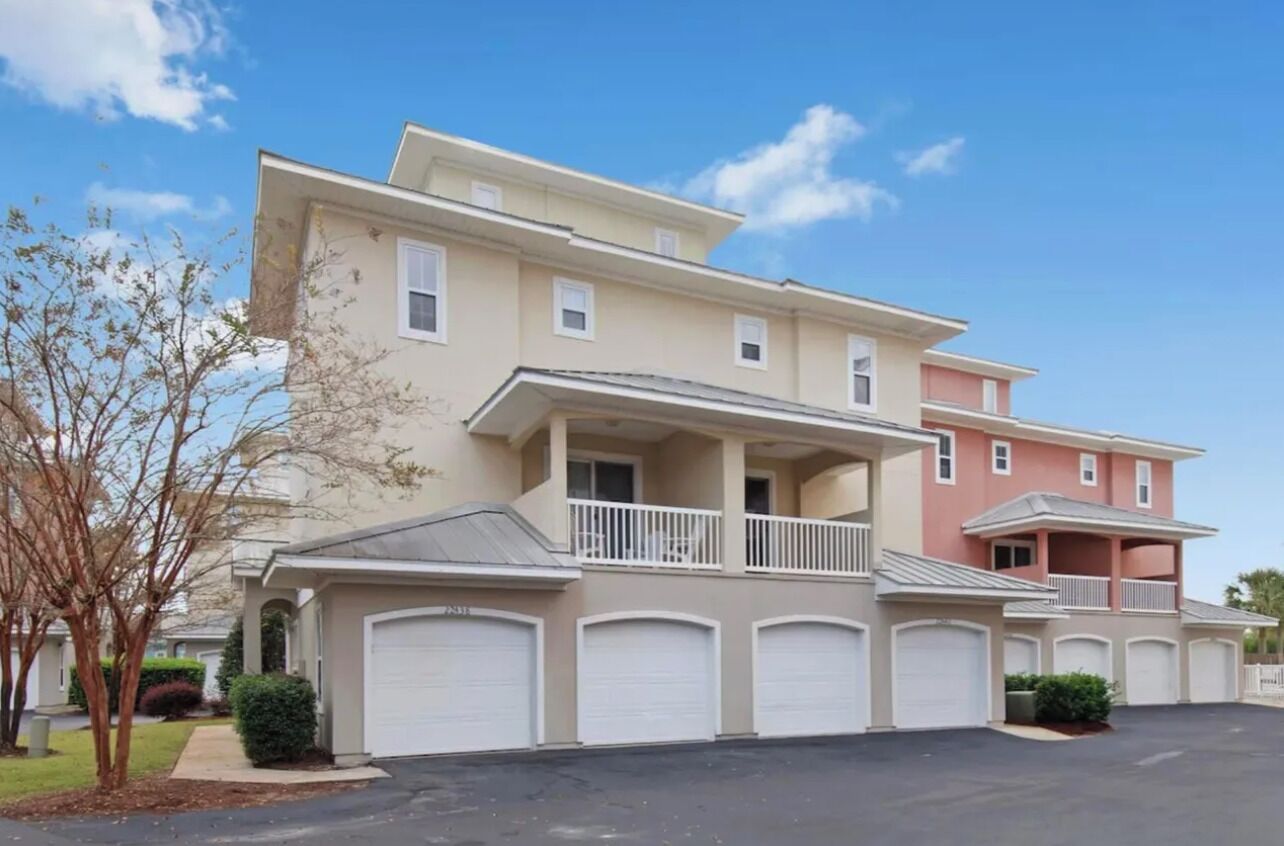 A multi-story residential building with a balcony, garage doors, and a clear sky.