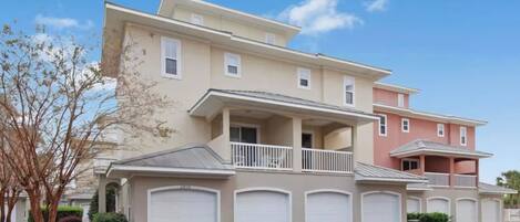 A multi-story residential building with a balcony, garage doors, and a clear sky.