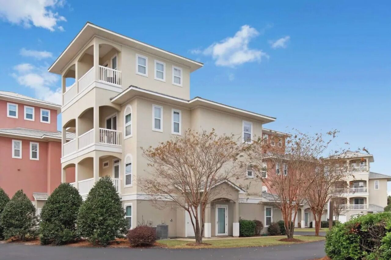 A multi-story residential building with balconies, a central entrance, and a parking area.