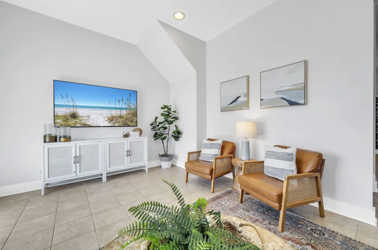 A spacious living area with a large flat-screen TV, two leather armchairs, a white cabinet, and a potted plant.