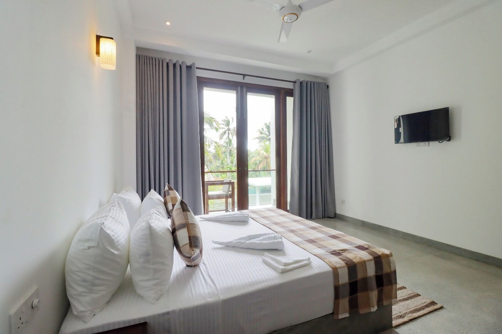 Un dormitorio con cama, cortinas, televisión y vista al balcón.