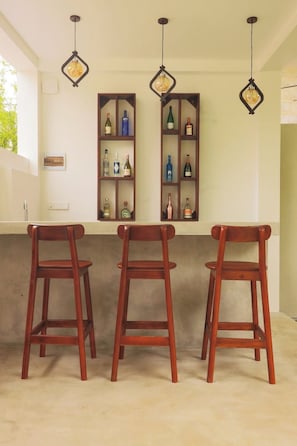 A bar area with three wooden bar stools, a wine rack with bottles, and pendant lights.