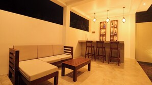 Una sala de estar moderna con un sofá, una mesa de centro de madera y una zona de bar con taburetes y estantes llenos de botellas.