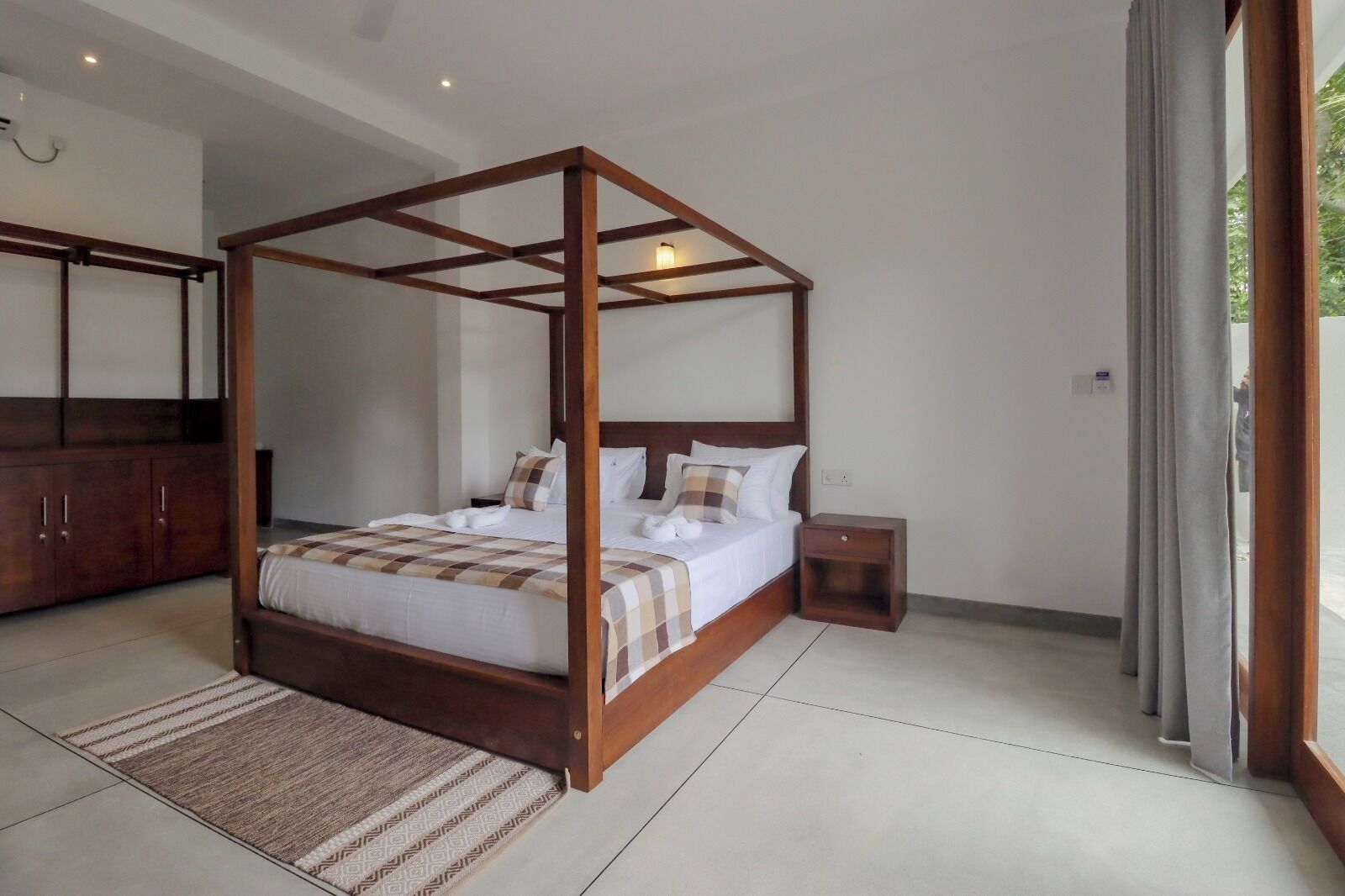 A four-poster bed with a checkered bedspread, a wooden nightstand, and a wardrobe.