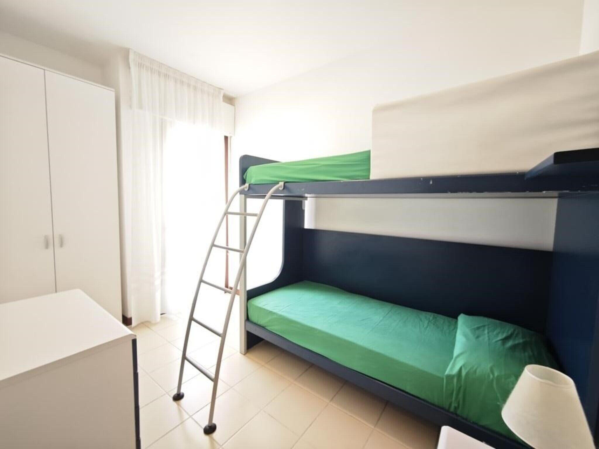 Ein Stockbett mit einer Leiter, einem Schreibtisch und einer Lampe in einem Zimmer mit einem Kleiderschrank und einem Fenster mit Vorhängen.