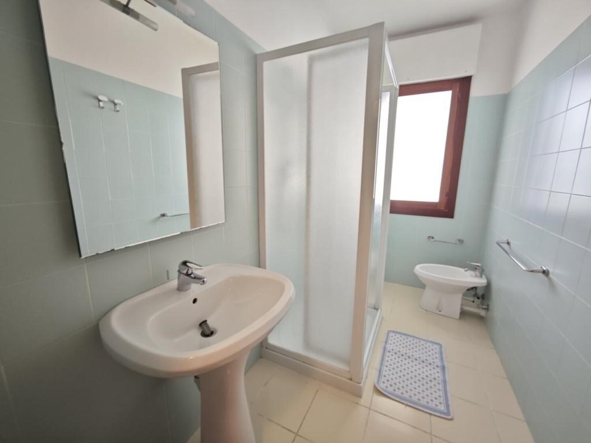 A bathroom with a pedestal sink, a toilet, a shower, and a window.