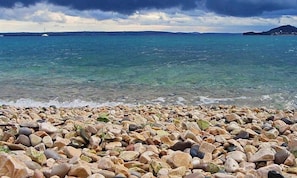 A pebble beach with clear water and a distant view of a lighthouse. - Amazing Place 4 Peaceful Holiday Apartman PIA (Poljana)