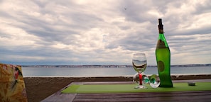 A table with a bottle and a glass, overlooking a body of water and a distant cityscape. - Amazing Place 4 Peaceful Holiday Apartman PIA (Poljana)