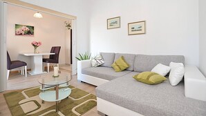 A modern living room with a grey sofa, a glass coffee table, a dining table with chairs, and a small plant. - Amazing Place 4 Peaceful Holiday L (Preko)