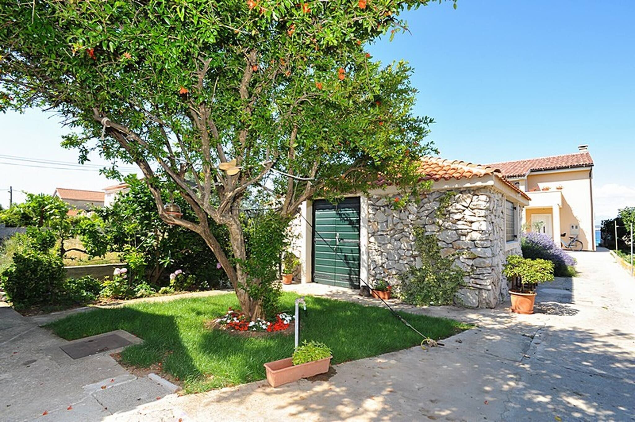A stone house with a green door, a tree in the front yard, and a clear sky.