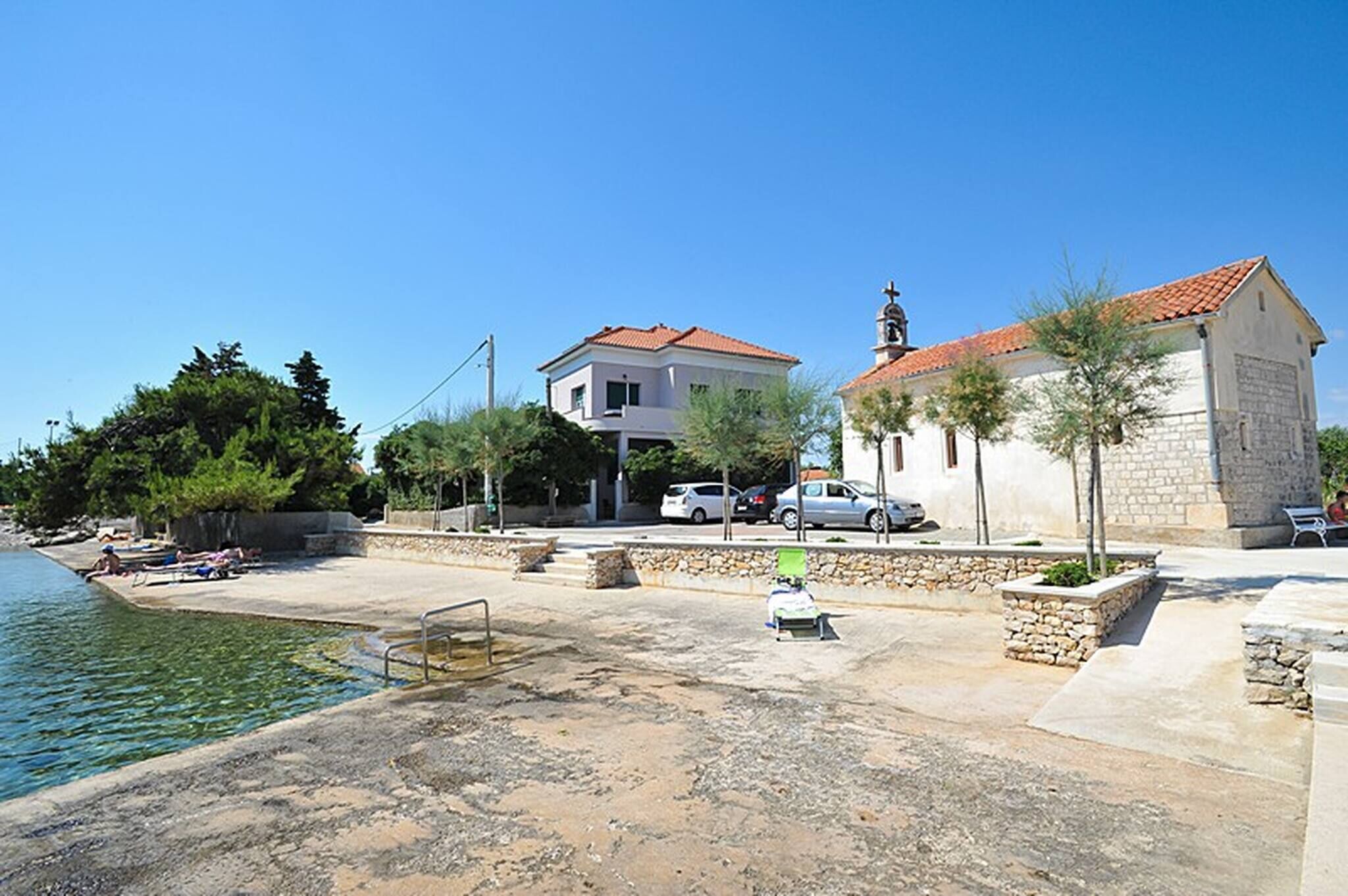 A waterfront property with a swimming pool, a stone wall, and a building with a red-tiled roof.