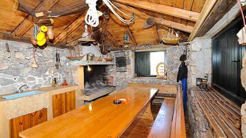 A rustic cabin interior with a stone fireplace, wooden benches, and a long wooden table.