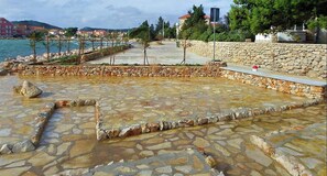 Ein mit Steinplatten gepflasterter Bereich mit einer Steinmauer und Blick aufs Meer.