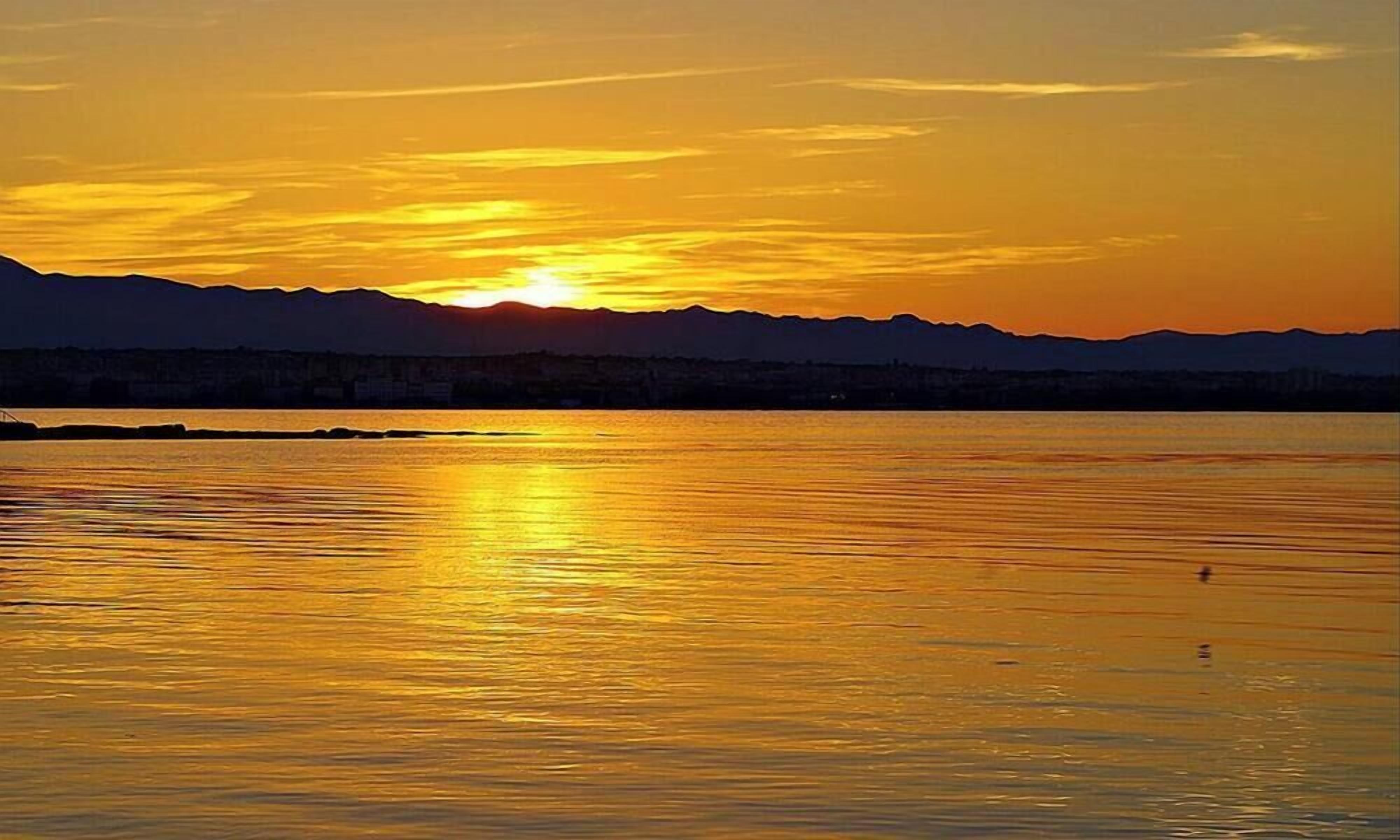 A sunset over a calm body of water with mountains in the background.