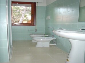 Casa de banho com duas sanitas, uma pia e uma janela.
