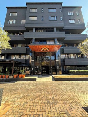 Un edificio a più piani con un design architettonico moderno, caratterizzato da un ingresso centrale con una tettoia in legno e un'area d'accesso in mattoni.