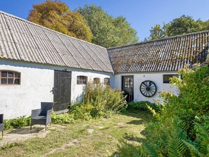 A traditional white building with a corrugated metal roof, a wooden wheel, and a garden area with ferns.