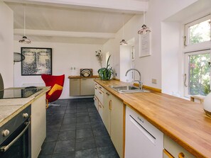 A modern kitchen with a wooden countertop, a sink, a dishwasher, and a red chair.