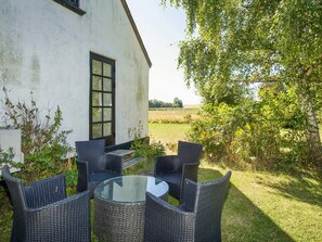 A white building with a large window and a glass table surrounded by wicker chairs.