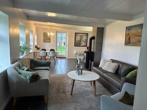 A living room with a sofa, armchair, coffee table, and a fireplace. There is a dining area with chairs and a table. - 4 Star Holiday Home in Sejero (Sejero)