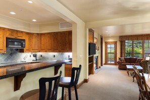 A kitchen with wooden cabinets, a microwave, and a sink. There is a living area with a couch, chairs, and a television. - Outpost: Grand View 3120 - Has A/C! (Jackson)