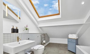 A modern bathroom with a skylight, a bathtub, a sink, and a toilet. - Flat -12 (London)