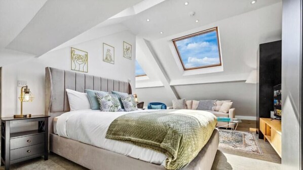 A bedroom with a bed, bedside tables, a nightstand, a sofa, a TV, and a window. - Flat -12 (London)