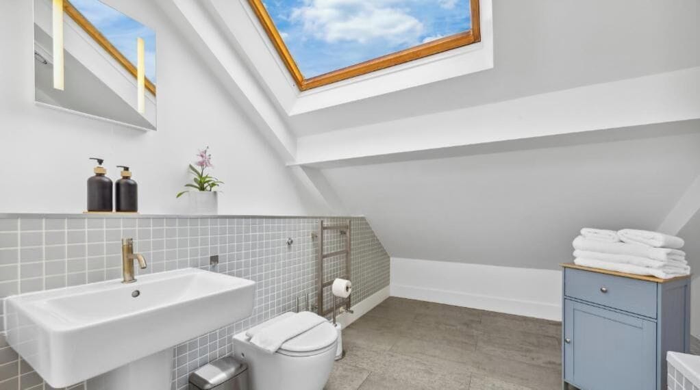 Une salle de bain moderne dotée d’un puits de lumière, d’un grand lavabo, de toilettes et d’un meuble de rangement.